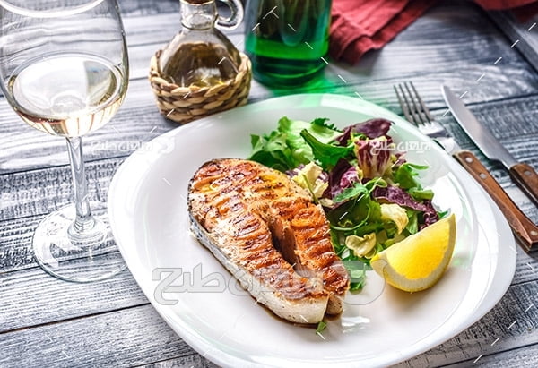 غذای کباب گوشت ماهی و لیمو و سالاد و سبزیجات، چنگال و چاقو